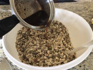 pouring mixture on dry granola in bowl